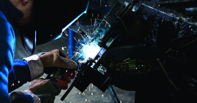 Welder at work on a steel fabrication, with sparks from the weld