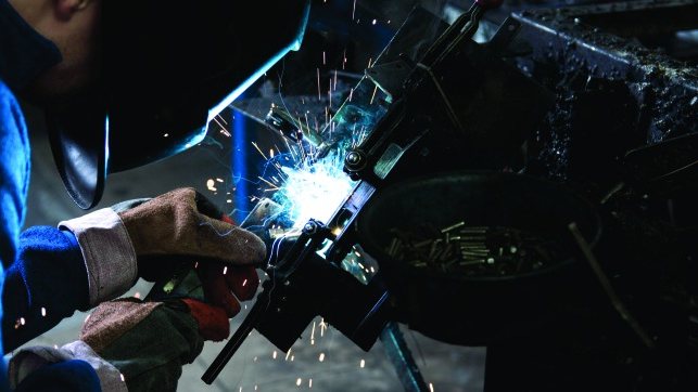 Welder at work on a steel fabrication, with sparks from the weld